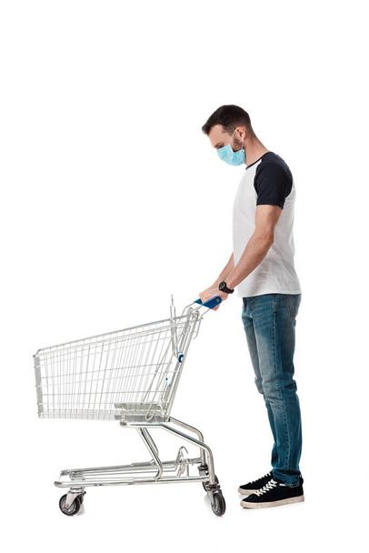 man in medical mask standing with empty shopping cart isolated on white - Foto, immagini