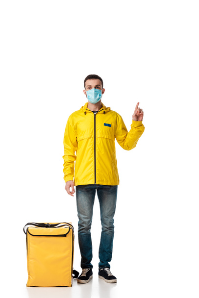 repartidor en máscara médica de pie cerca de la bolsa con la orden y señalando con el dedo en blanco
  - Foto, imagen