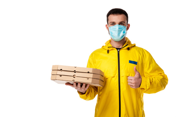 delivery man in medical mask holding pizza boxes and showing thumb up isolated on white  - Foto, Imagen
