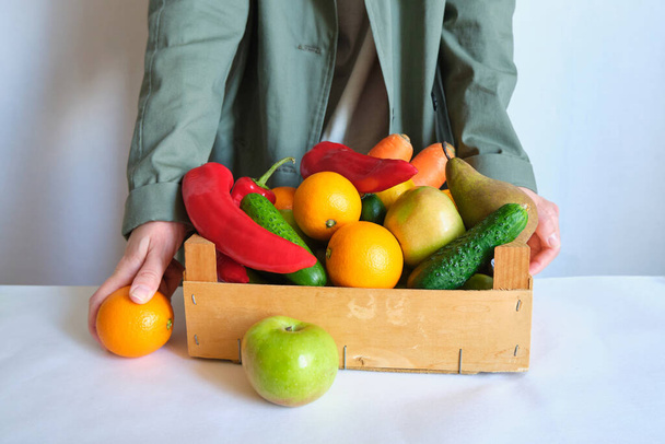 Woman in trench coat holding wooden box with natural fresh vegetables and fruits. Healthy eating, bio organic food. Shopping at grocery store. Female diet. Vegetarian lifestyle. Product for cooking - Photo, Image