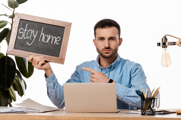 bebaarde freelancer wijzend met vinger naar krijtbord met thuis te blijven belettering geïsoleerd op wit  - Foto, afbeelding