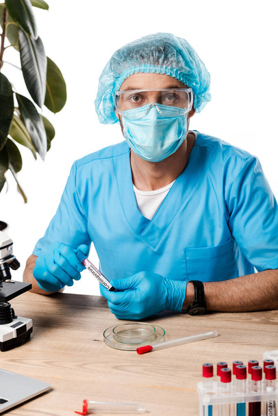 scientifique en casquette médicale et lunettes tenant tube à essai avec lettrage coronavirus près du microscope isolé sur blanc
  - Photo, image