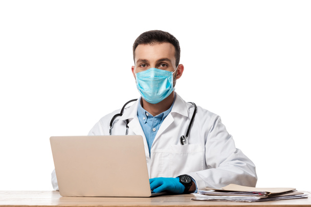 γιατρός με ιατρική μάσκα και λευκό παλτό χρησιμοποιώντας φορητό υπολογιστή που απομονώνονται σε λευκό  - Φωτογραφία, εικόνα