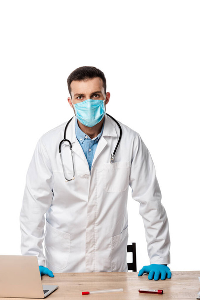 doctor in medical mask and white coat standing near test tubes with blood isolated on white  - Fotoğraf, Görsel