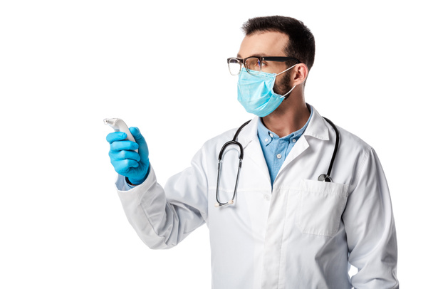 Arzt in medizinischer Maske und weißem Kittel mit kontaktlosem Pyrometer isoliert auf weiß  - Foto, Bild