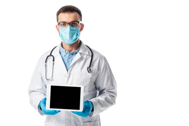 lékař v lékařské masce a bílém plášti s digitální tabletou s prázdnou obrazovkou izolovanou na bílém  - Fotografie, Obrázek