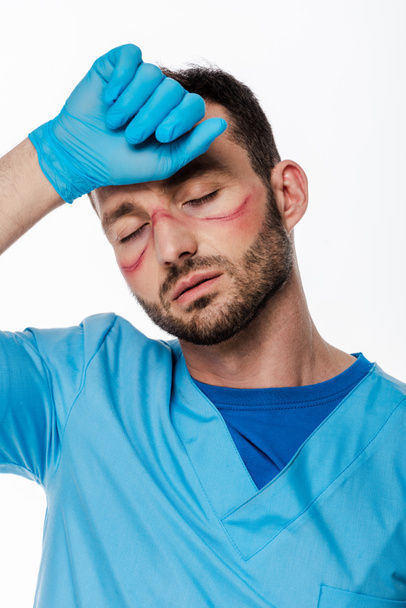 tired doctor with marks on face and closed eyes touching forehead isolated on white   - Fotoğraf, Görsel