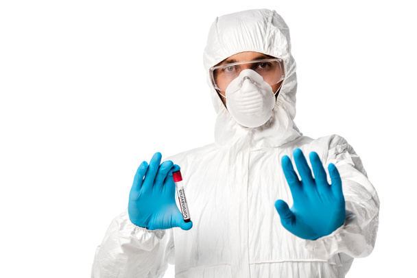 ハズマットスーツの男コロナウイルスの血液サンプルレタリングと白い上に隔離された停止標識を示すチューブを保持します  - 写真・画像