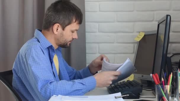 Mladý muž pracuje doma u počítače a listuje dokumenty. - Záběry, video