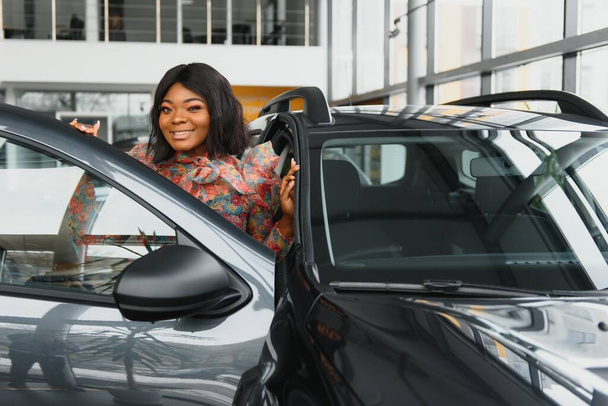 beautiful young african woman buying a car at dealership - Zdjęcie, obraz