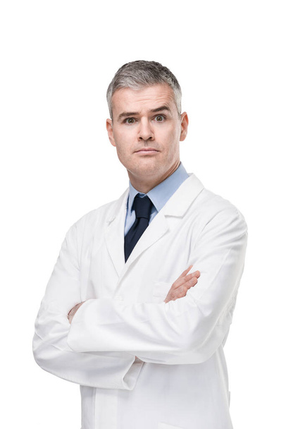 Confident doctor or pharmacist standing with folded arms staring intently at the camera with a penetrating look and serious expression isolated on white - Photo, Image