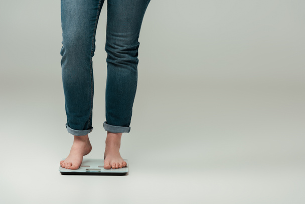 cropped view of plus size girl in jeans standing on scales on grey - Photo, Image