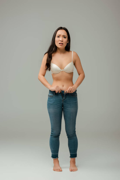 shocked and overweight asian girl wearing jeans on grey - Valokuva, kuva