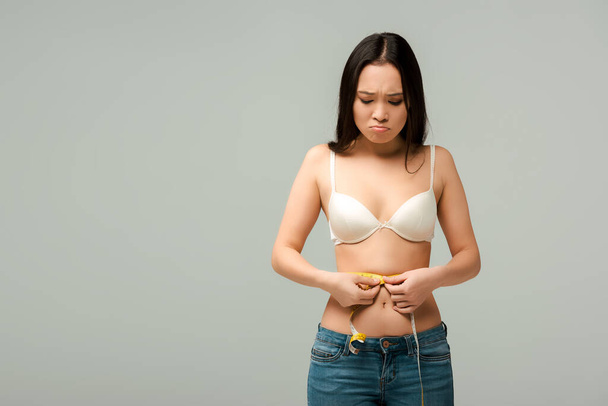 disgustado y con sobrepeso asiático chica medición cintura aislado en gris
  - Foto, imagen