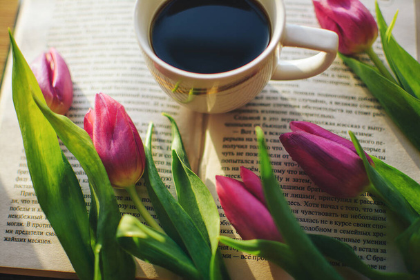 Forte caffè aromatico gustoso sulla finestra con un libro interessante e tulipani rosa. Il sole del mattino splende su un libro e caffè aromatico, e bellissimi tulipani rosa freschi si trovano nelle vicinanze
 - Foto, immagini
