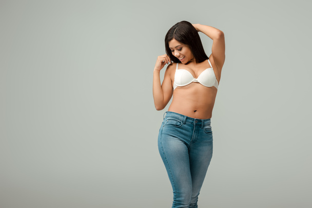 overweight and happy african american woman in jeans and bra standing isolated on grey - Foto, Bild