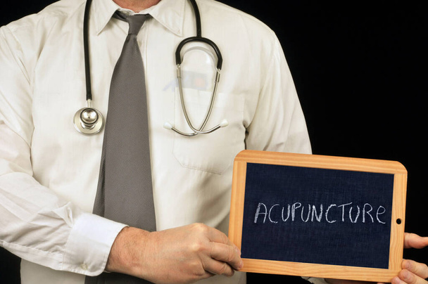 Doctor sosteniendo una pizarra escolar en la que se escribe acupuntura
  - Foto, Imagen