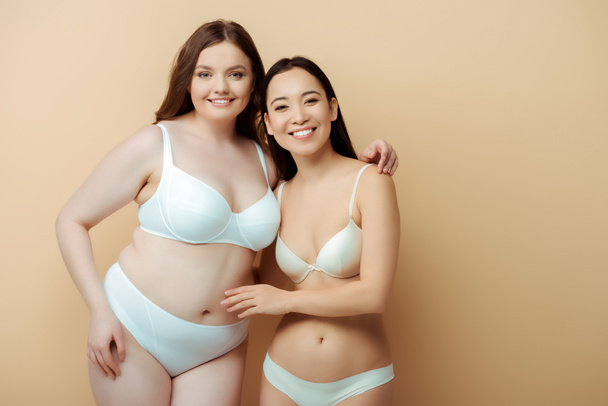plus size vrouw glimlachen met aziatisch meisje in ondergoed geïsoleerd op beige, lichaam positief concept  - Foto, afbeelding