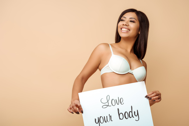 happy african american woman holding placard with love your body lettering isolated on beige  - Zdjęcie, obraz