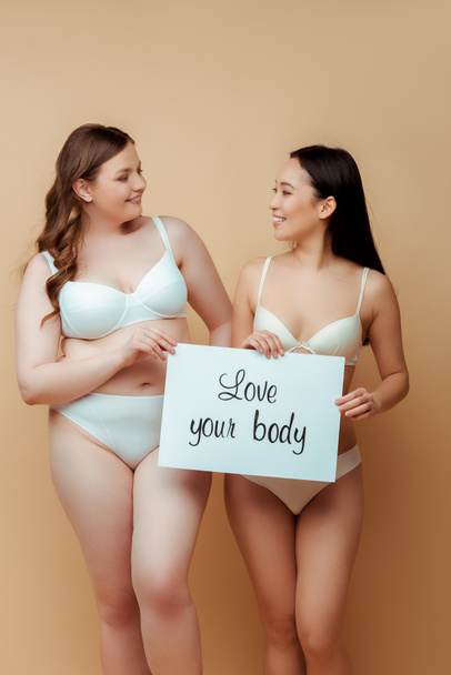 alegre multicultural niñas en ropa interior celebración cartel con amor su cuerpo letras aislado en beige, cuerpo concepto positivo
  - Foto, Imagen