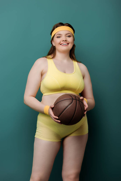 Plus size sportswoman with ball smiling and looking at camera on green - Foto, Imagem