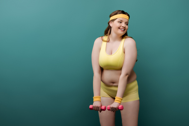 Plus size sportswoman training with dumbbells and smiling on green - Φωτογραφία, εικόνα