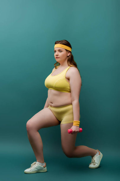 Plus size sportswoman training with dumbbells on green background - Foto, imagen