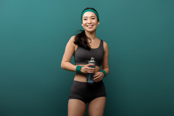 Вид спереди женщины со спортивной бутылкой, улыбающейся на зеленом
 - Фото, изображение