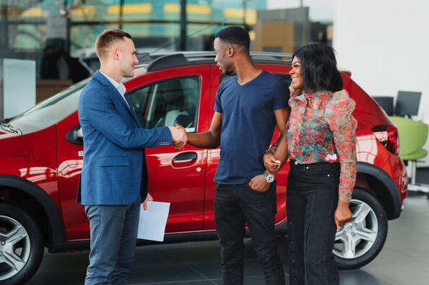 salesman showing new car to african couple in showroom - Foto, Bild