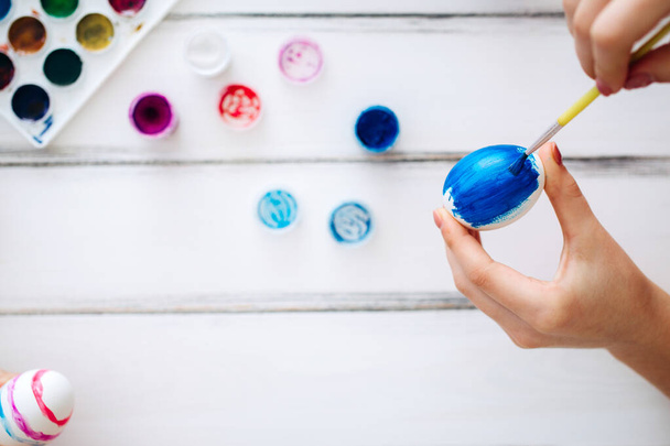 Закройте женские руки голубые пасхальные яйца Белый фон. Домашняя традиция рисования яиц
 - Фото, изображение