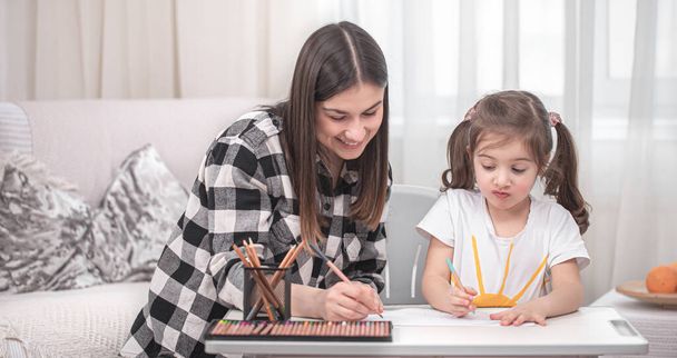 Egy anya egy gyerekkel az asztalnál ül és házi feladatot csinál. A gyerek otthon tanul. Otthoni tanulás. A szöveg helye. - Fotó, kép