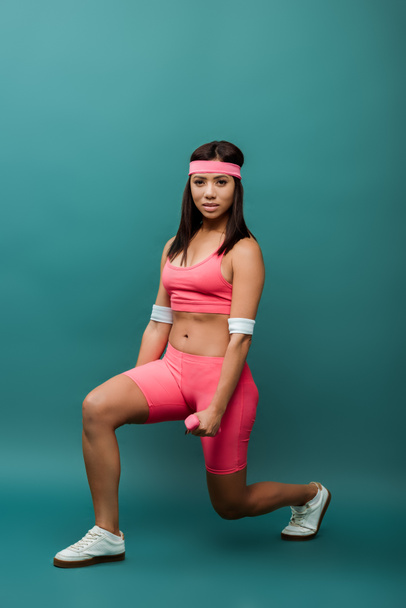 African american sportswoman doing lunges with dumbbells and looking at camera on green  background - Fotografie, Obrázek