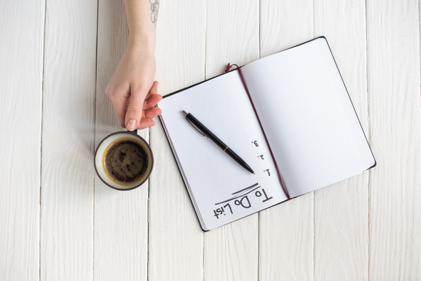 Vista ritagliata della donna che tiene una tazza di caffè vicino al notebook con scritte e penna su sfondo di legno
 - Foto, immagini