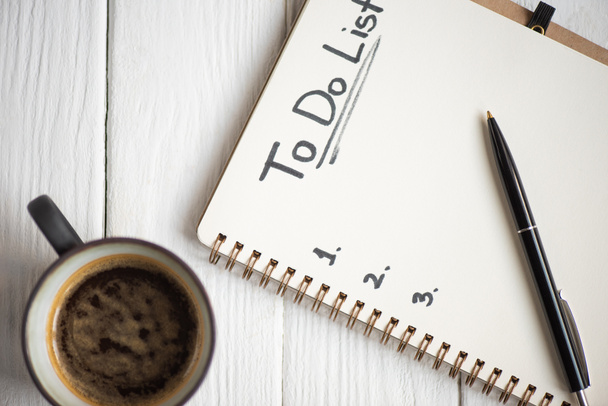 Vista superior do notebook com letras da lista de tarefas e caneta com xícara de café em fundo de madeira
 - Foto, Imagem