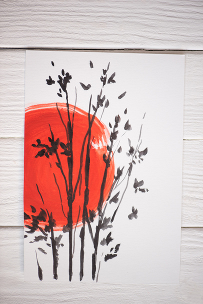 Top view of paper with Japanese painting with red sun and branches on wooden background - Photo, Image