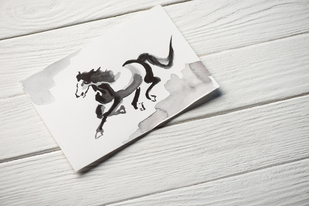 Bovenaanzicht van papier met Japanse schilderkunst met paard op houten ondergrond - Foto, afbeelding