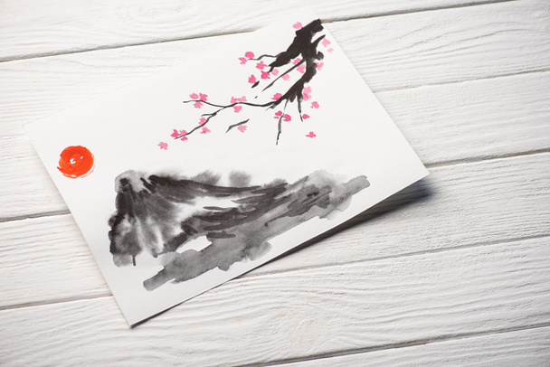 High angle view of paper with japanese painting with sun, Sakura branches and grey hill on wooden background - Photo, Image