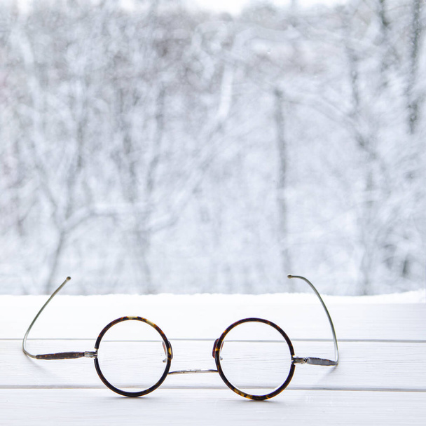 Vintage ronde leesbril op een witte vensterbank tegen de achtergrond van een winterbos - Foto, afbeelding