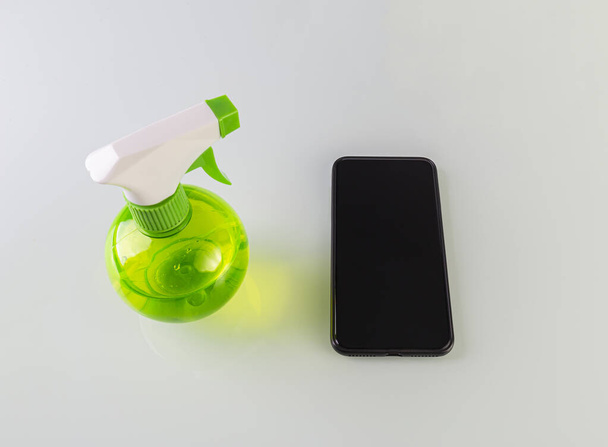 Sanitizing Sprayflasche und ein schwarzes Smartphone isoliert auf weißem Hintergrund. Hausreinigung gegen Coronavirus verhindern - Foto, Bild