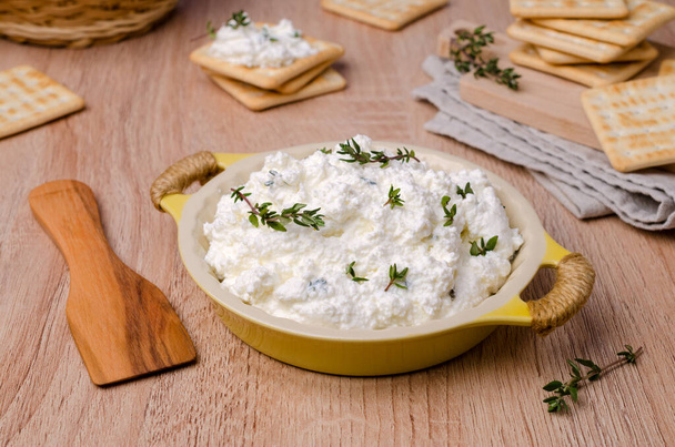 Traditional soft cheese with thyme and crackers on a wooden background. Selective focus. - Photo, Image