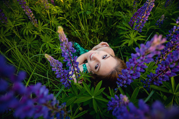 Jeune belle fille assise dans des lupins violets dans un champ dans l'herbe. Concept de la nature. La vue du haut
. - Photo, image