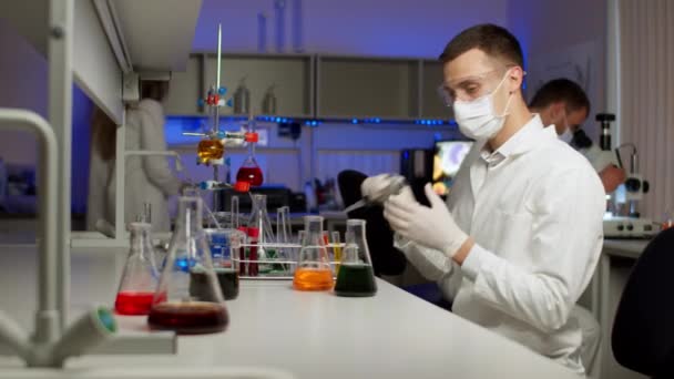 Jonge wetenschapper mengen gekleurde vloeistoffen - Video