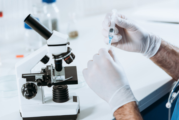 partial view of biologist in latex gloves holding syringe near microscope - Valokuva, kuva