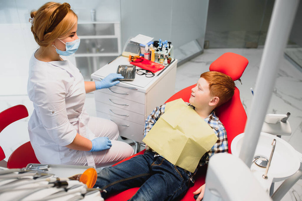 Dentist wearing mask. Red-haired child dentist wearing mask examining cute boy - Photo, Image