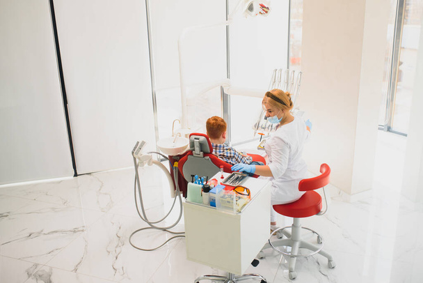 Dentysta dziecięcy badający małe męskie zęby na krześle dentystycznym w klinice dentystycznej - Zdjęcie, obraz
