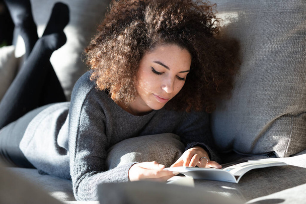 Une jolie jeune femme allongée sur un salon moderne lisant un magazine
. - Photo, image