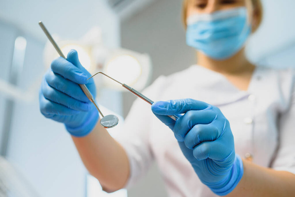Портрет стоматолога, держащего в руках стоматологические инструменты в клинике крупным планом
 - Фото, изображение