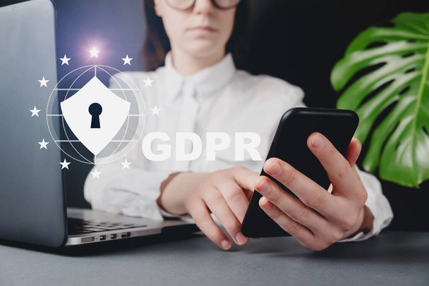 Cyber internet security concept. GDPR and cybersecurity. Protection of private personal data. Close up front view young woman holding smartphone, sitting at desk near pc. Data Protection Regulation. - Фото, зображення