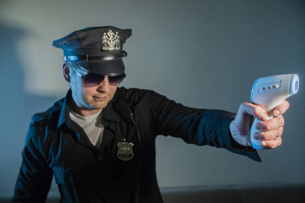 полицейский в полицейском костюме проверяет температуру дистанционно, держит инфракрасный термометр, детектирует температуру для людей от вируса короны инфекции
 - Фото, изображение