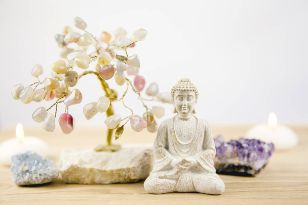 Kalmerende meditatie achtergrond met zittende mediterende Boeddha, kristallen clusters (paarse amethist en blauwe hemelse) en edelsteen draad boom wit minimalistische achtergrond met kopieerruimte. - Foto, afbeelding